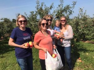 Four adults and a baby standing in an apple orchard.